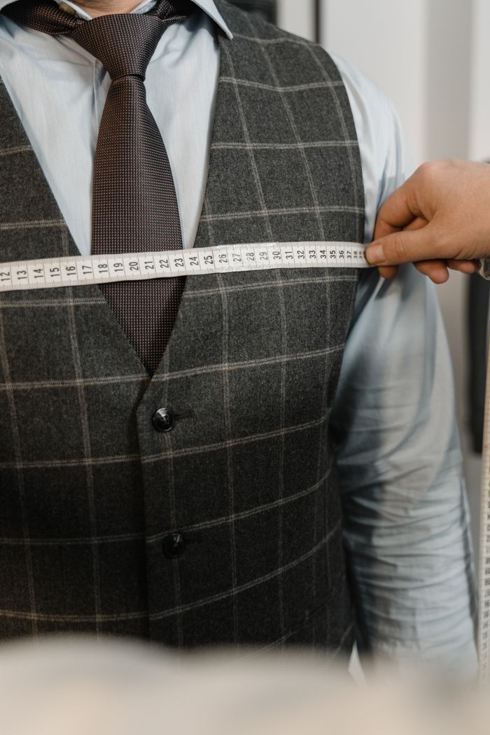 about-us Tailor measuring client's chest for a tailored suit in an atelier setting.